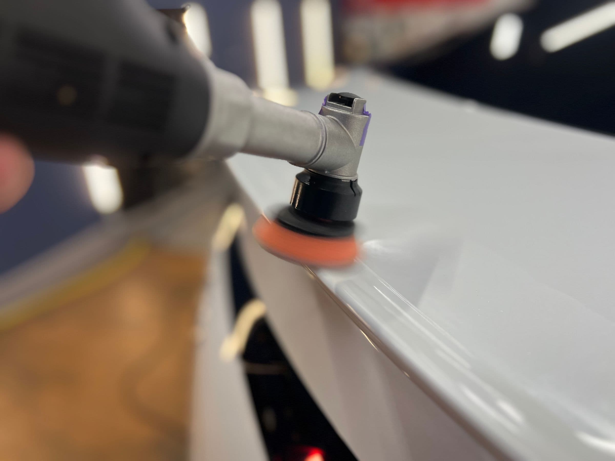 Poliermaschine mit Schwammteller auf einer hellen Motorhaube